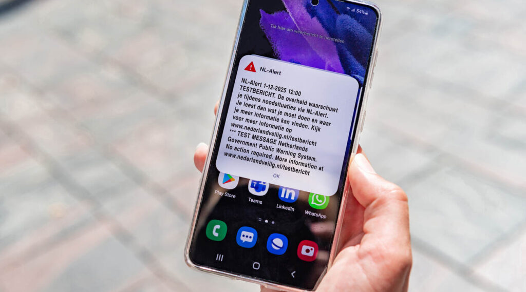 Een telefoon in iemands hand met waarop het NL-Alert testbericht van 1 december 2025 te zien is.