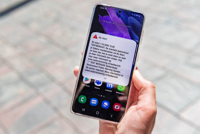 Een telefoon in iemands hand met waarop het NL-Alert testbericht van 1 december 2025 te zien is.