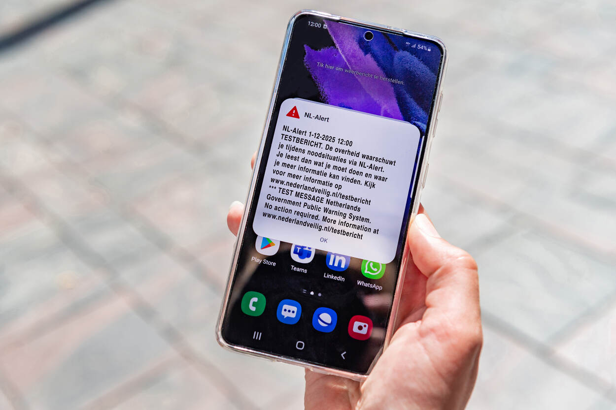 Een telefoon in iemands hand met waarop het NL-Alert testbericht van 1 december 2025 te zien is.