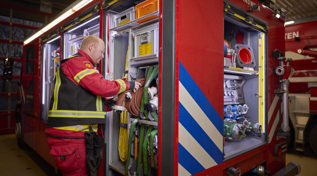 brandweerman die een branweerslang gaat uitrolt uit de brandweerauto.