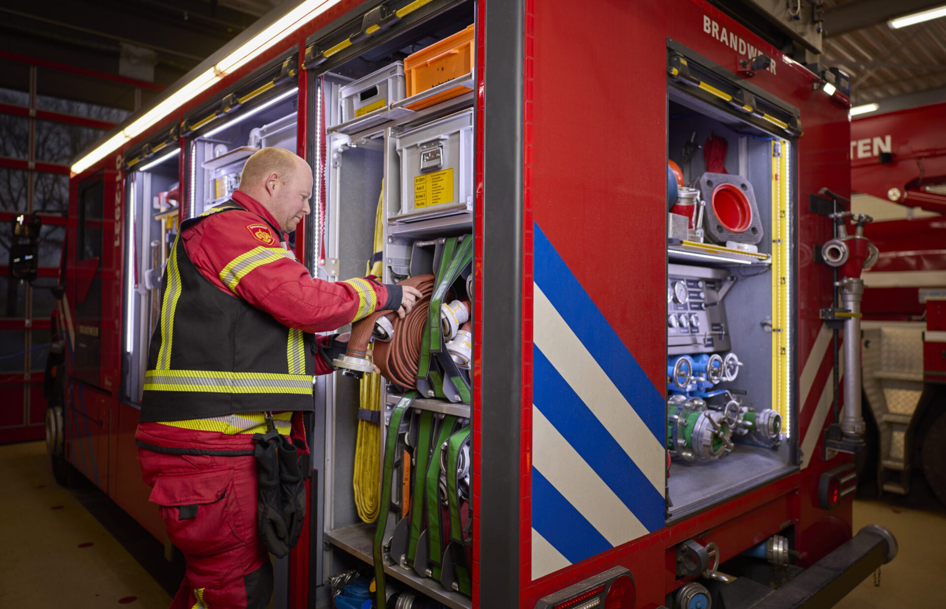 brandweerman die een branweerslang gaat uitrolt uit de brandweerauto.
